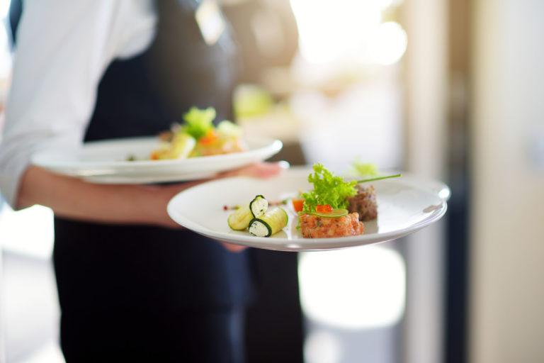 Waiter carrying plates with meat dish on some festive event