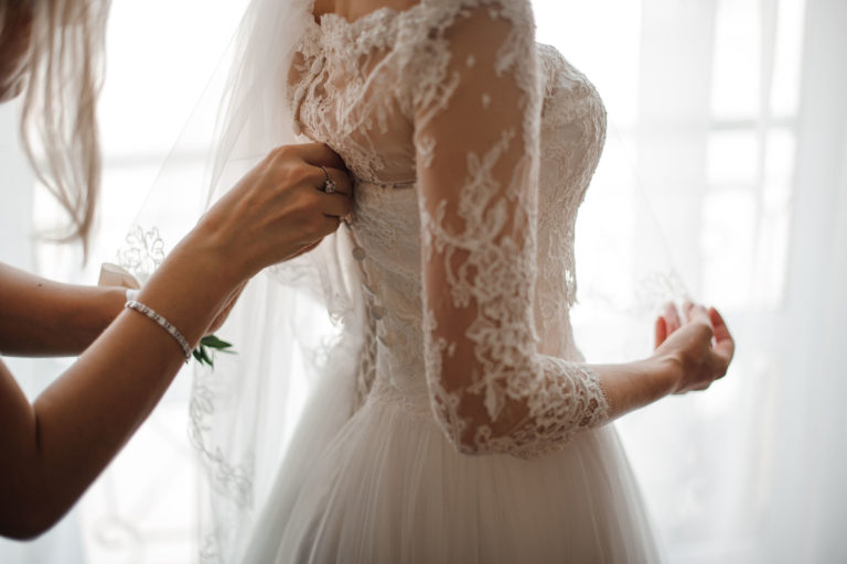 Bridesmaid making bow-knot on the back of brides wedding dress Bridesmaid making bow-knot on the back of brides wedding dress